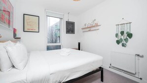 A bedroom with a bed, a radiator, and wall decorations including framed pictures and a hanging plant.