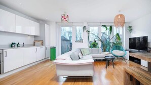 A modern living room with a sofa, a television, and a dining area.