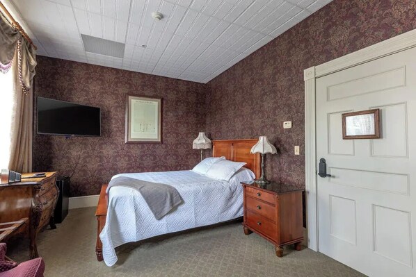 A bedroom with a bed, a dresser, a desk, a television, and a door. - Big Tree Treaty Room - Big Tree Inn

 (Geneseo)