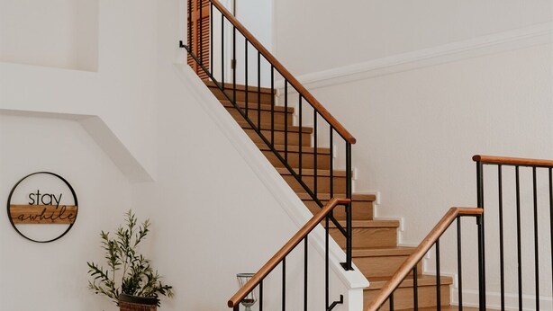Un salon moderne avec un escalier, un canapé blanc, une table basse et un panneau décoratif mural.