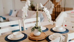 Une table à manger dressée avec de l’assiette blanche, des bols et un centre de table composé de fleurs blanches dans un pot blanc.
