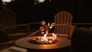 Un foyer extérieur de forme ronde, alimenté par des bûches, entouré de deux fauteuils Adirondack.