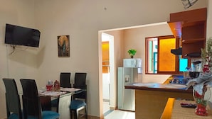Una cocina compacta con zona de comedor, un televisor montado en la pared y un refrigerador pequeño.
