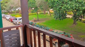 Un balcón con vista a un jardín ajardinado y coches estacionados.
