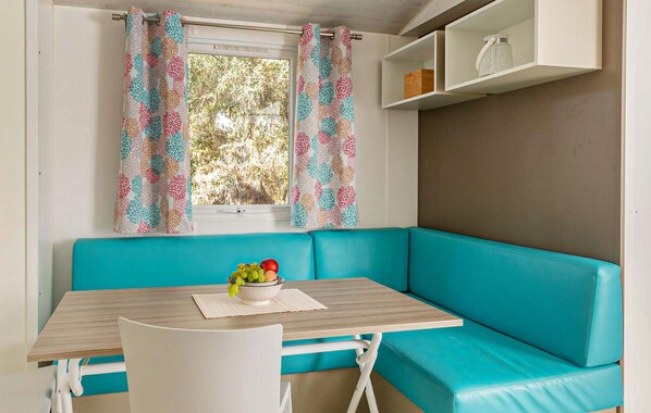 Un sofá color turquesa, una mesita de madera con un frutero, y una ventana con cortinas estampadas.
