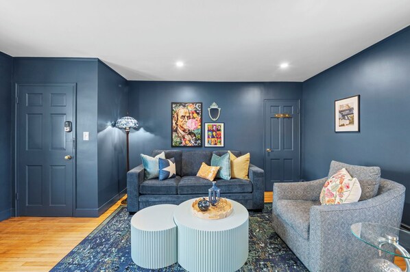 Un salon moderne aux murs bleu foncé, comprenant deux canapés, une table basse et des objets décoratifs.