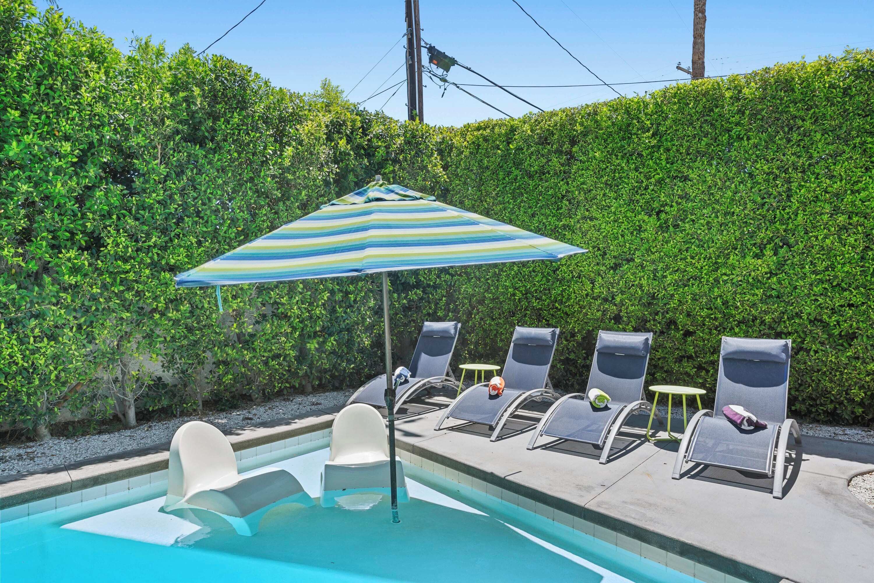 A swimming pool with lounge chairs and a striped umbrella.