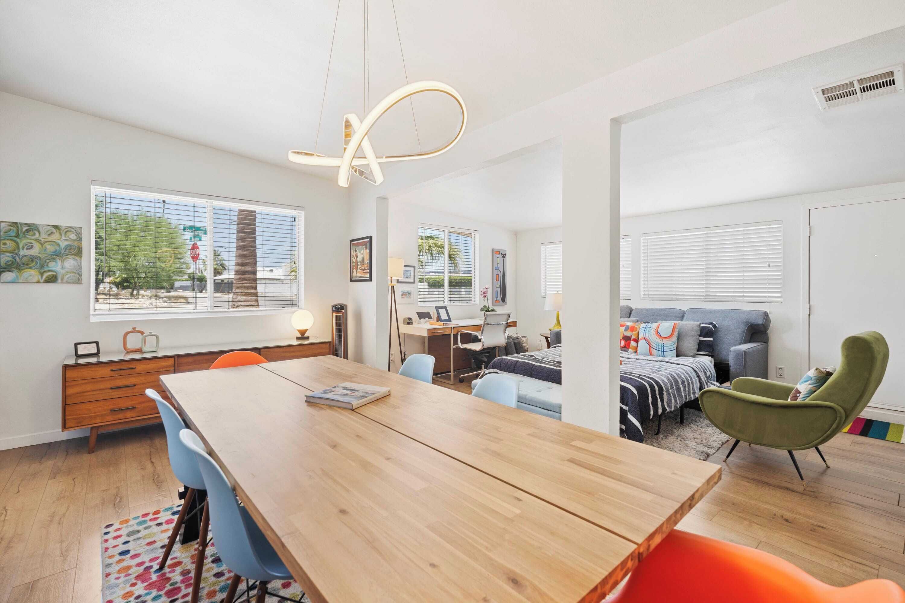 Un espace de vie moderne avec une table à manger en bois, des chaises bleues, un fauteuil vert et un lit recouvert d’une couverture à rayures.