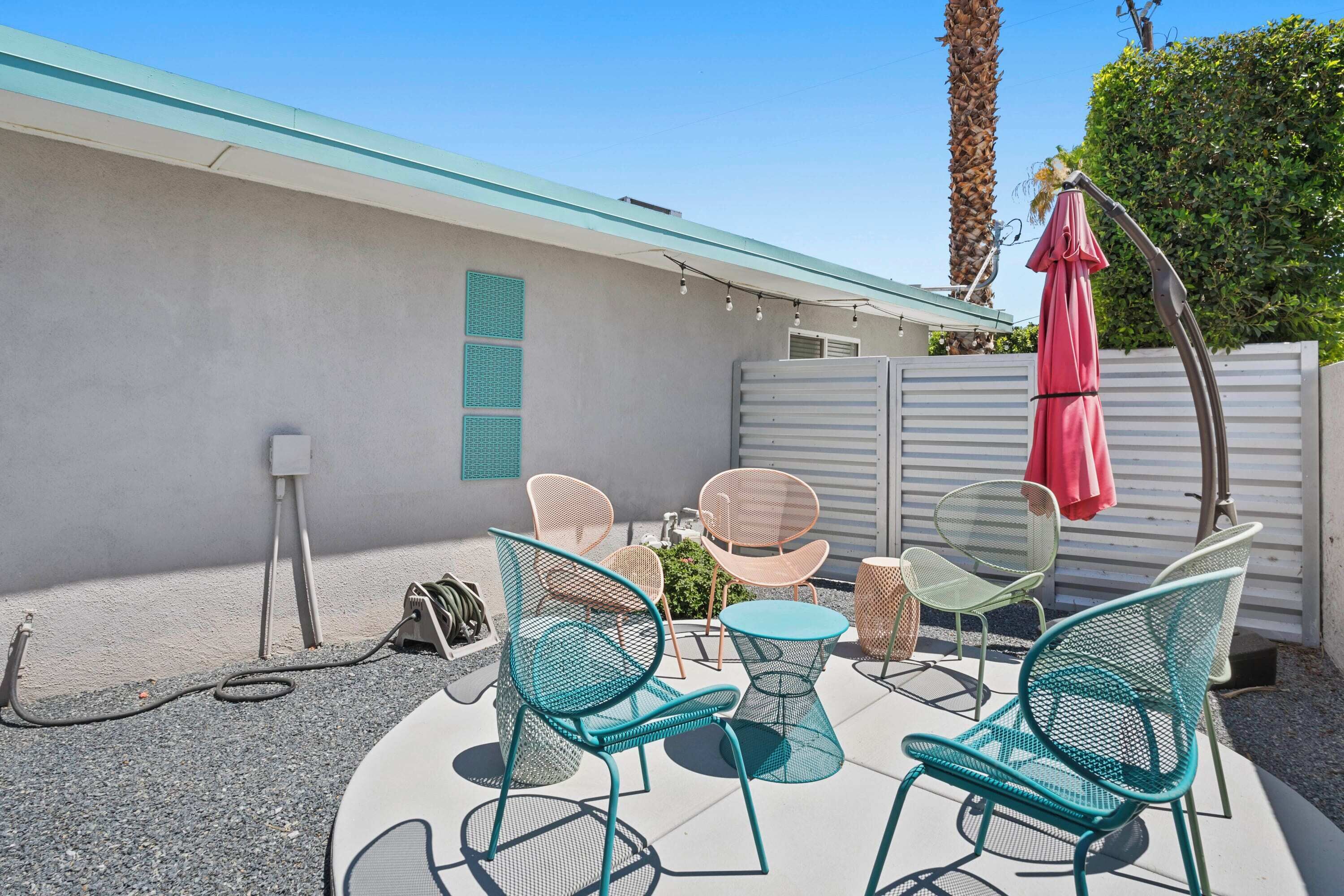 An outdoor patio with metal chairs and a table, a red umbrella, and a white fence.
