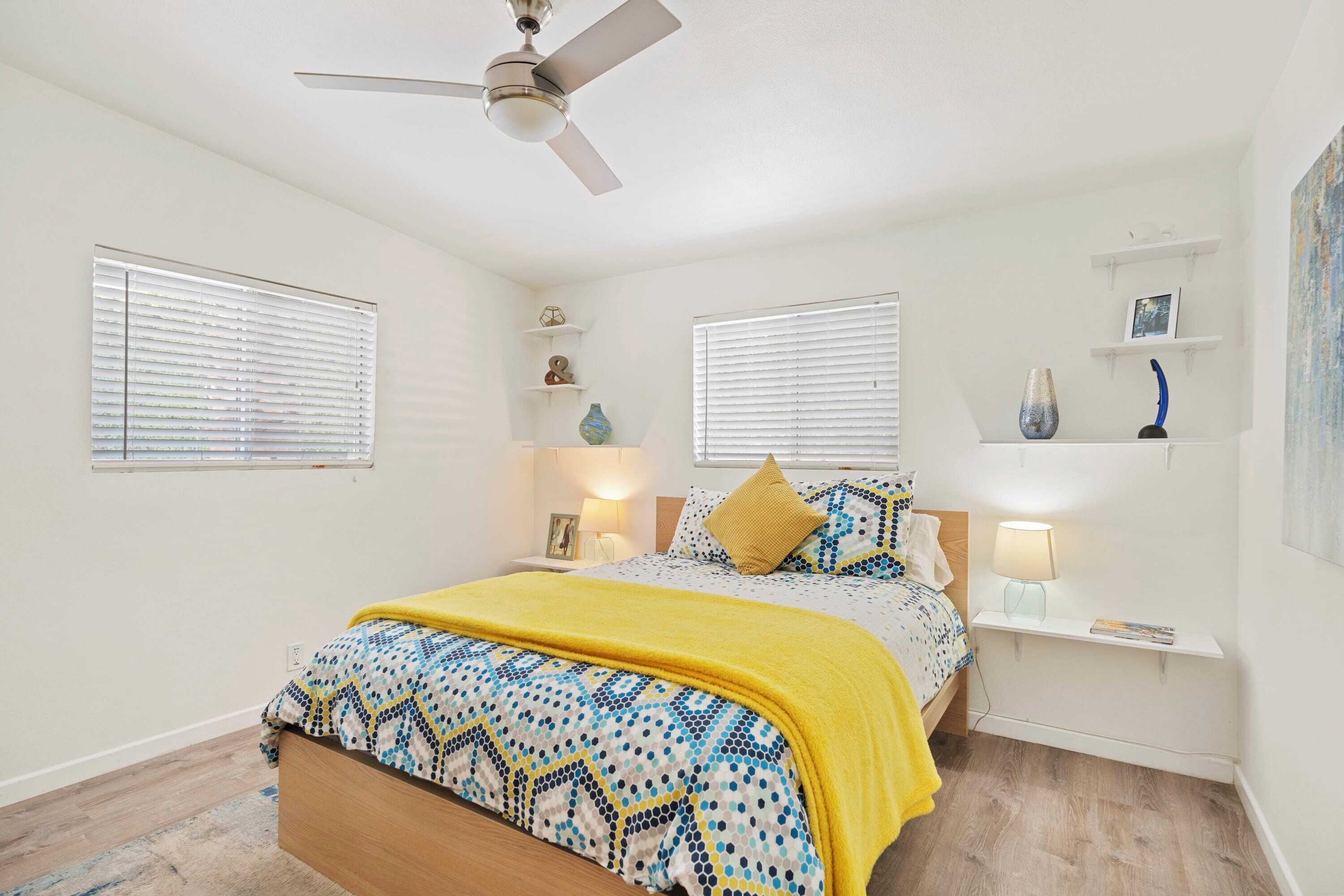A bedroom with a bed, bedside tables, a ceiling fan, and wall-mounted shelves.