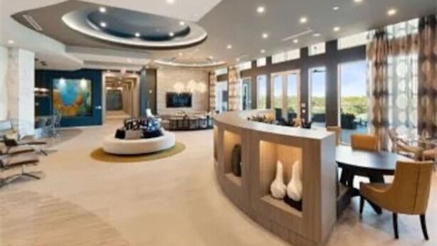 A spacious hotel lobby with a central reception desk, seating area, and a large window offering a view.