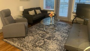A living room with a grey sofa, a glass coffee table with a vase, and a patterned rug.