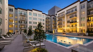 A modern hotel with a swimming pool, multiple balconies, and lounge areas.