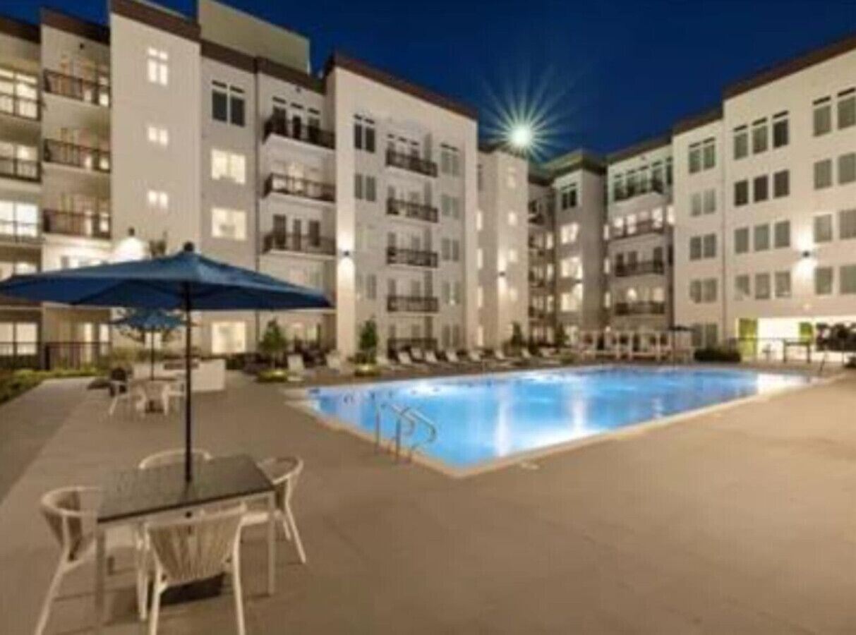 A swimming pool surrounded by a building with multiple balconies and a covered outdoor seating area.