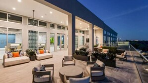 A modern outdoor lounge area with seating and planters, large windows, and a view of the cityscape. - Spacious 3B 2.5B Apt by Galleria (Houston)