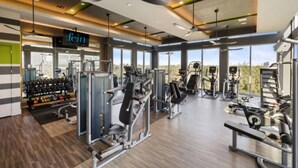 A modern gym with various exercise machines, large windows, and a visible cityscape. - Spacious 3B 2.5B Apt by Galleria (Houston)