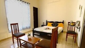 Ein Zimmer mit einem Bett, zwei Holzstühlen, einem kleinen Tisch und einem Fenster mit Vorhängen.