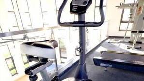 Ein Stepper in einem Fitnessstudio, mit einem digitalen Display und einer Hantelbank im Hintergrund.