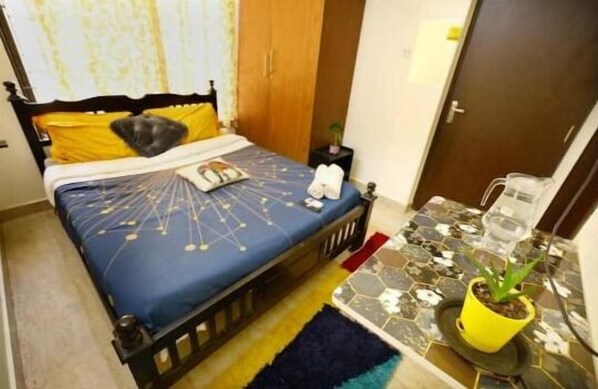 A bedroom with a bed, a nightstand, a potted plant, and a door. - Continental Lebe inn (vada nemmeli)