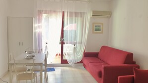 A room with a dining table, chairs, a red sofa, a white curtain, and a window with a view.