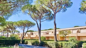 A row of beige apartment buildings with a well-maintained garden and trees in front.