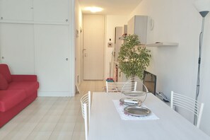 Un comedor con una mesa blanca, sillas y un sofá rojo. Hay una planta sobre la mesa y una puerta blanca al fondo.
