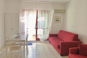 Una stanza con un tavolo da pranzo, sedie, un divano rosso, una tenda bianca e una finestra vista.