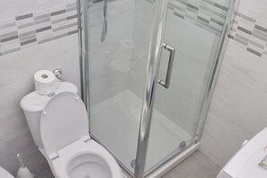 Un bagno moderno con doccia vetro, un water con portarotolo e pavimento piastrellato.