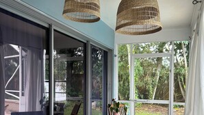 A room with a sliding glass door leading to an outdoor area, a wooden table with chairs, and two wicker pendant lights.
