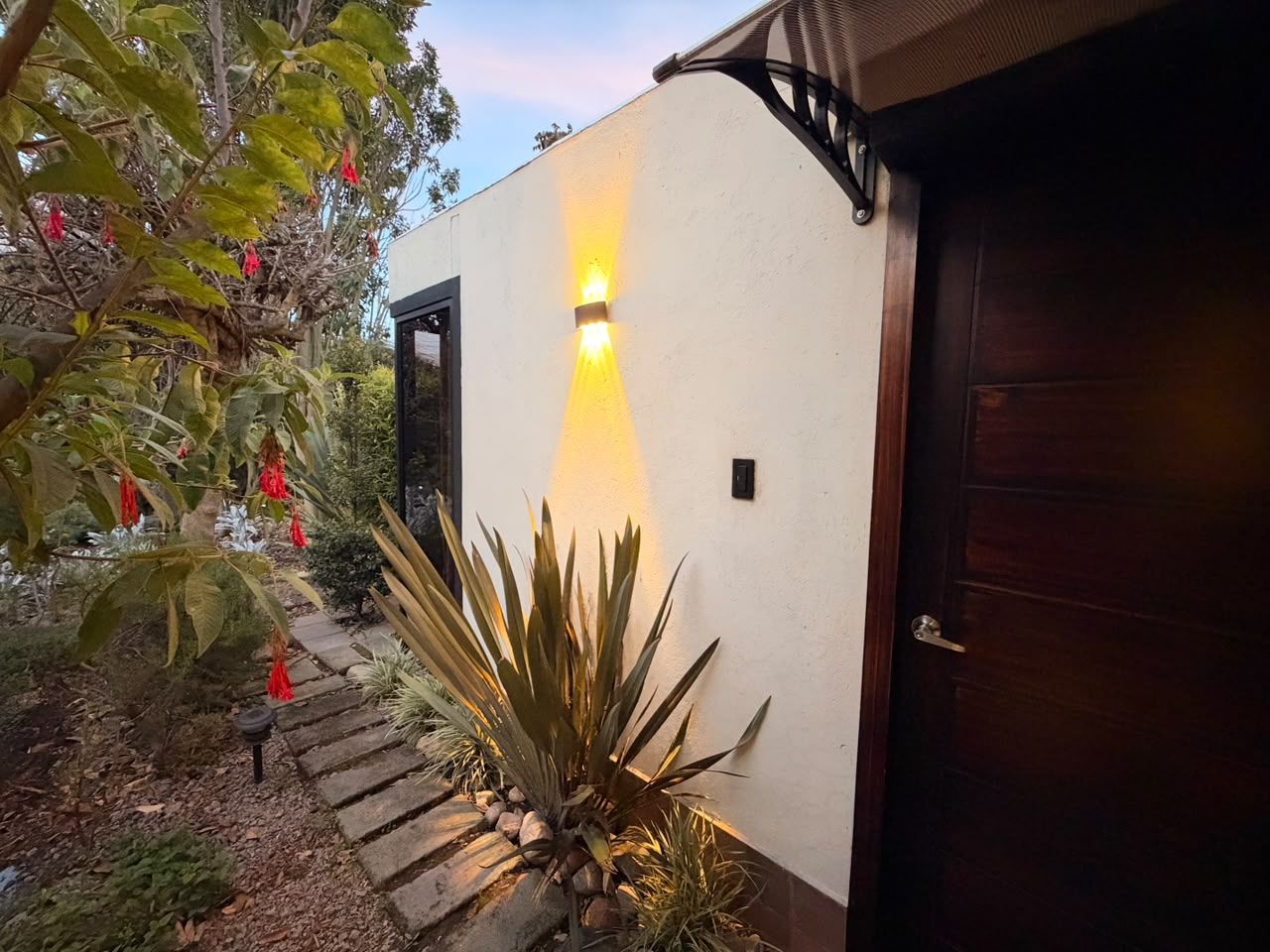 Fachada de una casa con un accesorio de luz, una puerta de madera y un camino de piedra.