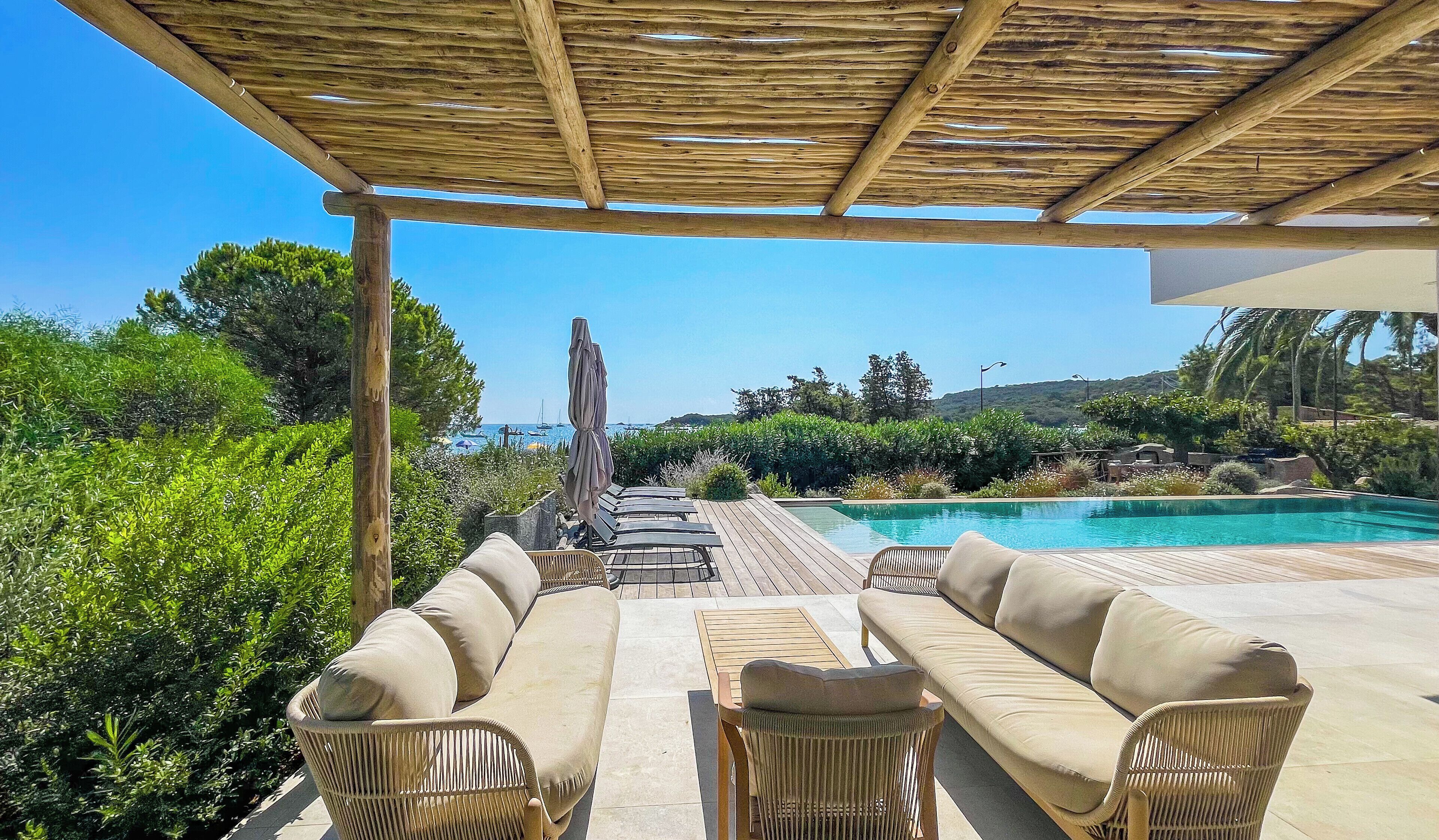 A covered outdoor seating area with a pool, wicker furniture, and a view of the sea.
