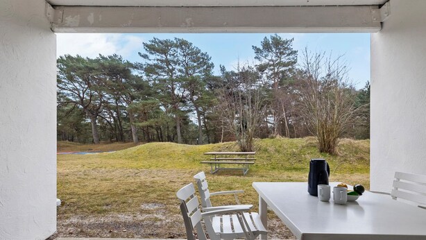 A patio area with a table and chairs, a picnic table, and a view of a grassy area with trees.