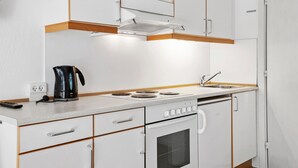 A compact kitchenette with a stove, oven, sink, and a coffee maker.