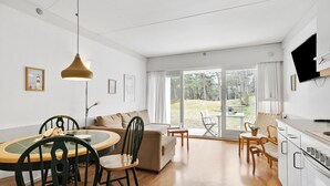 A modern, well-lit room with a dining area, sofa, and a view of a garden through large sliding doors.