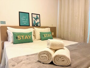 A hotel room with a bed, two pillows with 'STAY' text, a framed 'VIVE! Gai da do casulo STAY' sign, and a rolled towel on the bed. - STAY Metropolitan Barcelona  (Goiania)