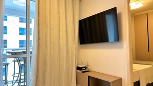 A hotel room with a large window, a flat-screen TV mounted on the wall, a small bedside table, and a bed with a white bedspread. - STAY Metropolitan Barcelona  (Goiania)