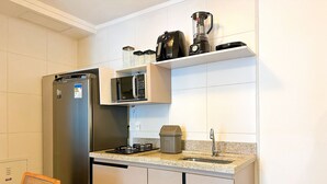 A compact kitchen with a refrigerator, microwave, stove, sink, and a coffee maker on the countertop. - STAY Metropolitan Barcelona  (Goiania)