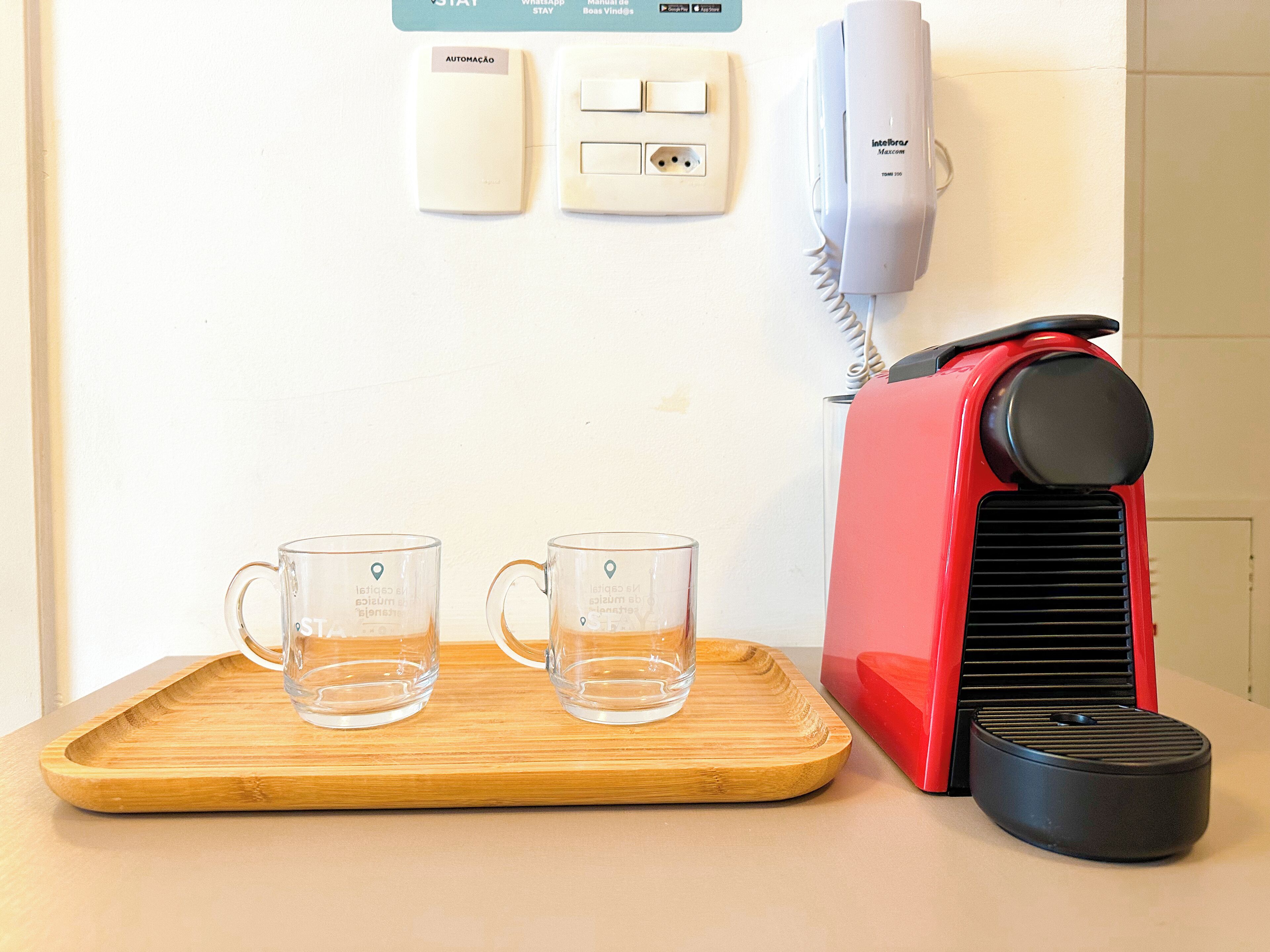 Un comptoir de cuisine avec une cafetière rouge, deux tasses en verre transparent et un plateau en bois.