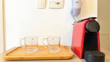 Un comptoir de cuisine avec une cafetière rouge, deux tasses en verre transparent et un plateau en bois.