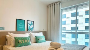 A hotel room with a bed, pillows with "STAY" text, a framed picture, and a window with a city view. - STAY Metropolitan Barcelona  (Goiania)