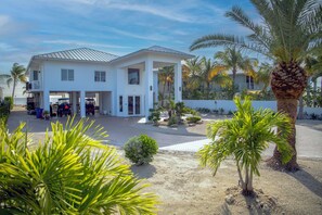 Une maison à deux étages dotée d’un patio couvert, de palmiers et d’une allée enrobée de sable.