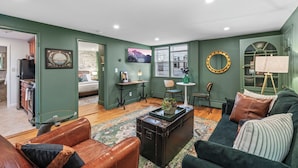 A living room with a green wall, a wooden floor, a leather sofa, a glass coffee table, and a large window.