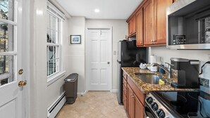 A compact kitchen with white walls, wooden cabinets, a granite countertop, and stainless steel appliances.