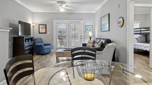Un salon avec une table en verre, un ventilateur de plafond, un téléviseur et un canapé.