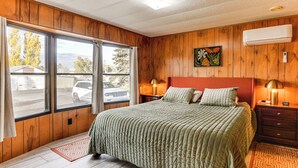 Une chambre avec un grand lit, des murs en bois, une fenêtre avec des rideaux, une table de chevet et un climatiseur fixé au mur.