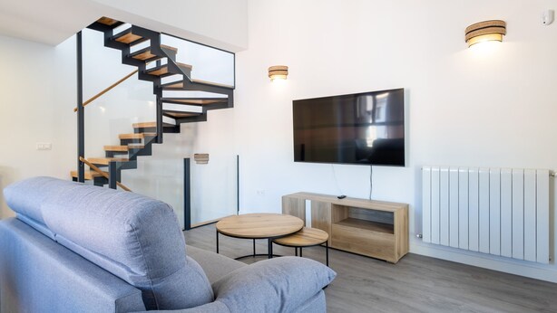 Un salon moderne avec un canapé gris, un escalier en bois, un téléviseur à écran plat et un radiateur blanc.