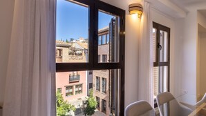Une pièce dotée de grandes fenêtres, d’une table en verre et offrant une vue sur les bâtiments environnants.