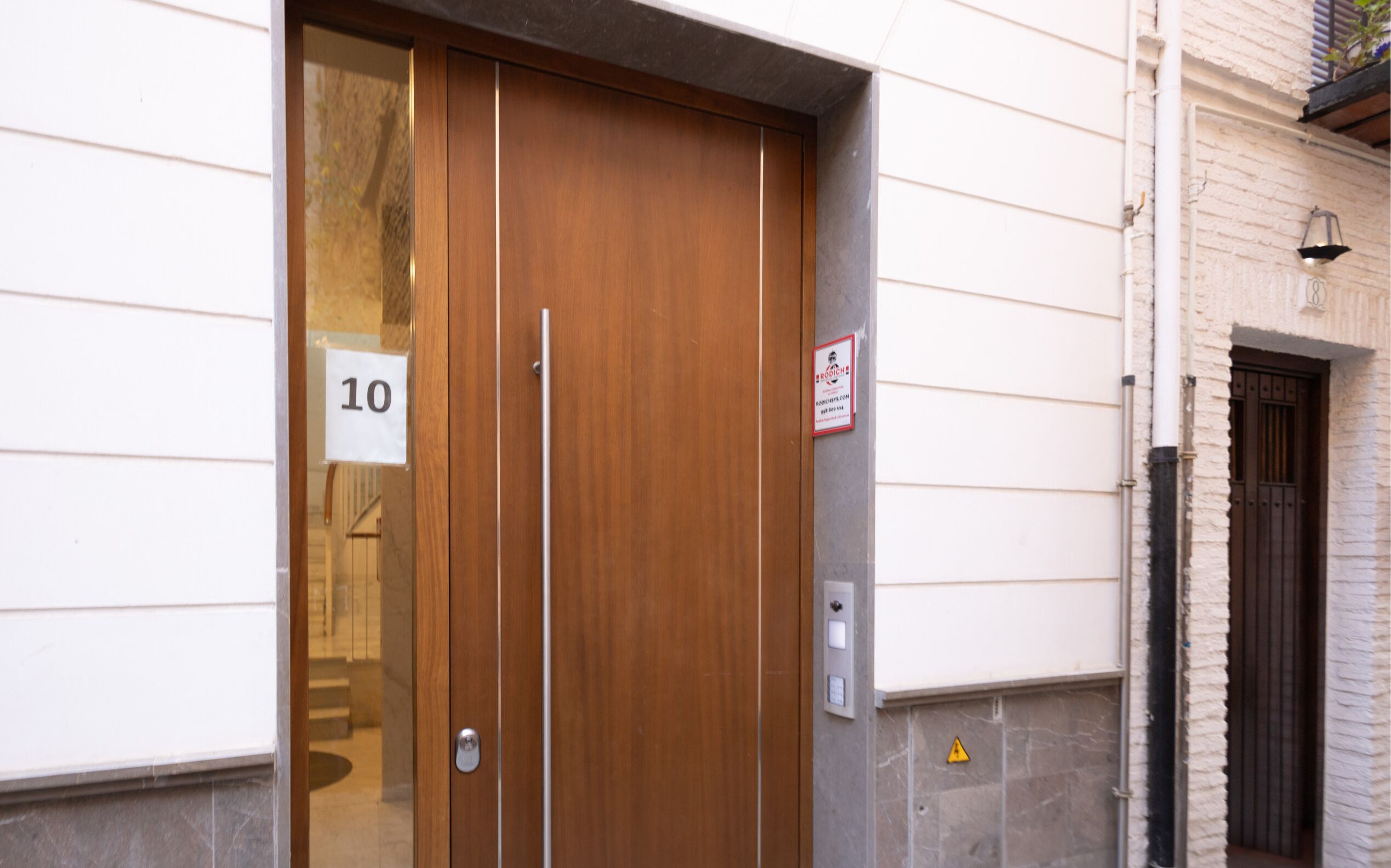 Une porte en bois avec une plaque portant le numéro 10, un interphone et une petite pancarte fix ée au mur.