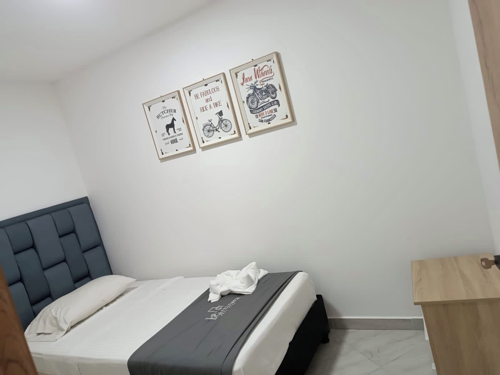 Une chambre à coucher avec un lit, une tête de lit, une table de chevet et trois affiches encadrées accrochées au mur.