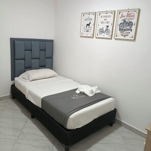 A single bed with a grey upholstered headboard and white bedding, a small white towel on the bed, and three framed posters on the wall. - Guayacan (Guatapé)